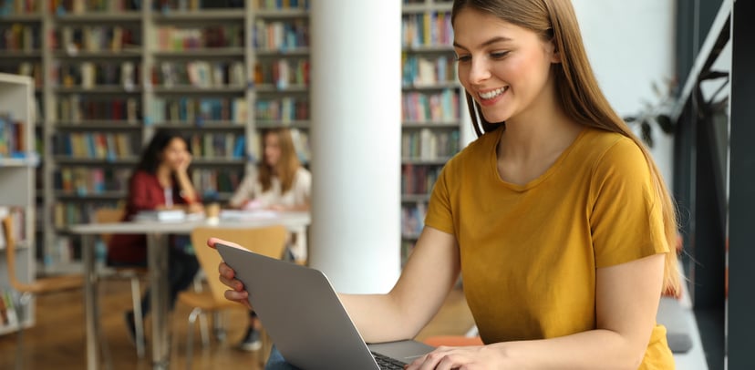 A young woman working on her laptop in a library. 