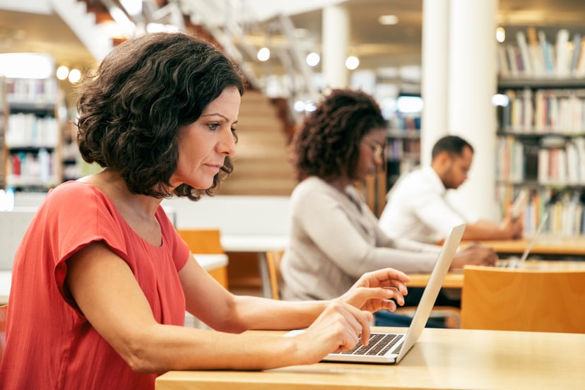 Adult students sitting at desks and using laptops