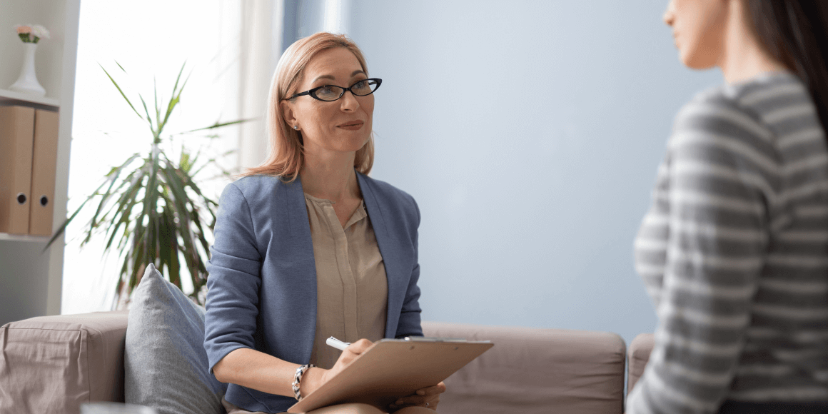 A clinical social worker listening attentively to her patient and taking notes on a clipboard.A clinical social worker listening attentively to her patient and taking notes on a clipboard.